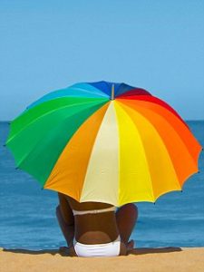 BDDDCE An attractive young African woman holding a multi coloured umbrella sitting on a sandy beach with a blue sea in the background.. Image shot 07/2009. Exact date unknown.